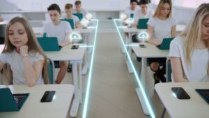 Estudiantes sentados en sus pupitres utilizando ordenadores portátiles en un aula. Líneas de neón digitales e iconos de nubes ilustran la conectividad y la tecnología, destacando un entorno moderno en el que conceptos como la verificación de edad en redes sociales son cada vez más relevantes.