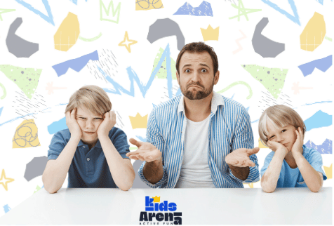 Un hombre sentado entre dos niños, todos con cara de aburrimiento o frustración, con los brazos levantados en un gesto de confusión. El fondo es colorido y abstracto, y en la parte inferior se ve el logotipo de Kids Arena.