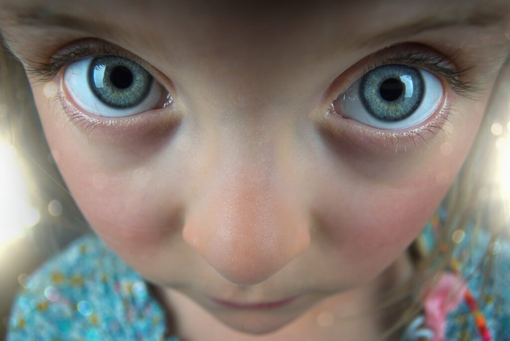 Extreme close-up of a child’s face with wide blue eyes and a curious expression, highlighting facial features. The child is looking directly at the camera, capturing the excitement often seen during active play at a kids activities Marbella center.
