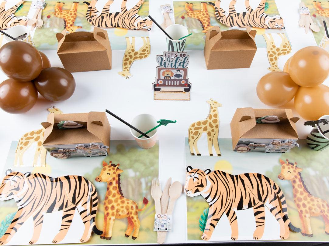 Una fiesta temática de safari con manteles individuales con jirafas y tigres, globos marrones, cajas de comida de cartón, utensilios de madera, animales de juguete y un centro de mesa Lets Go Wild.